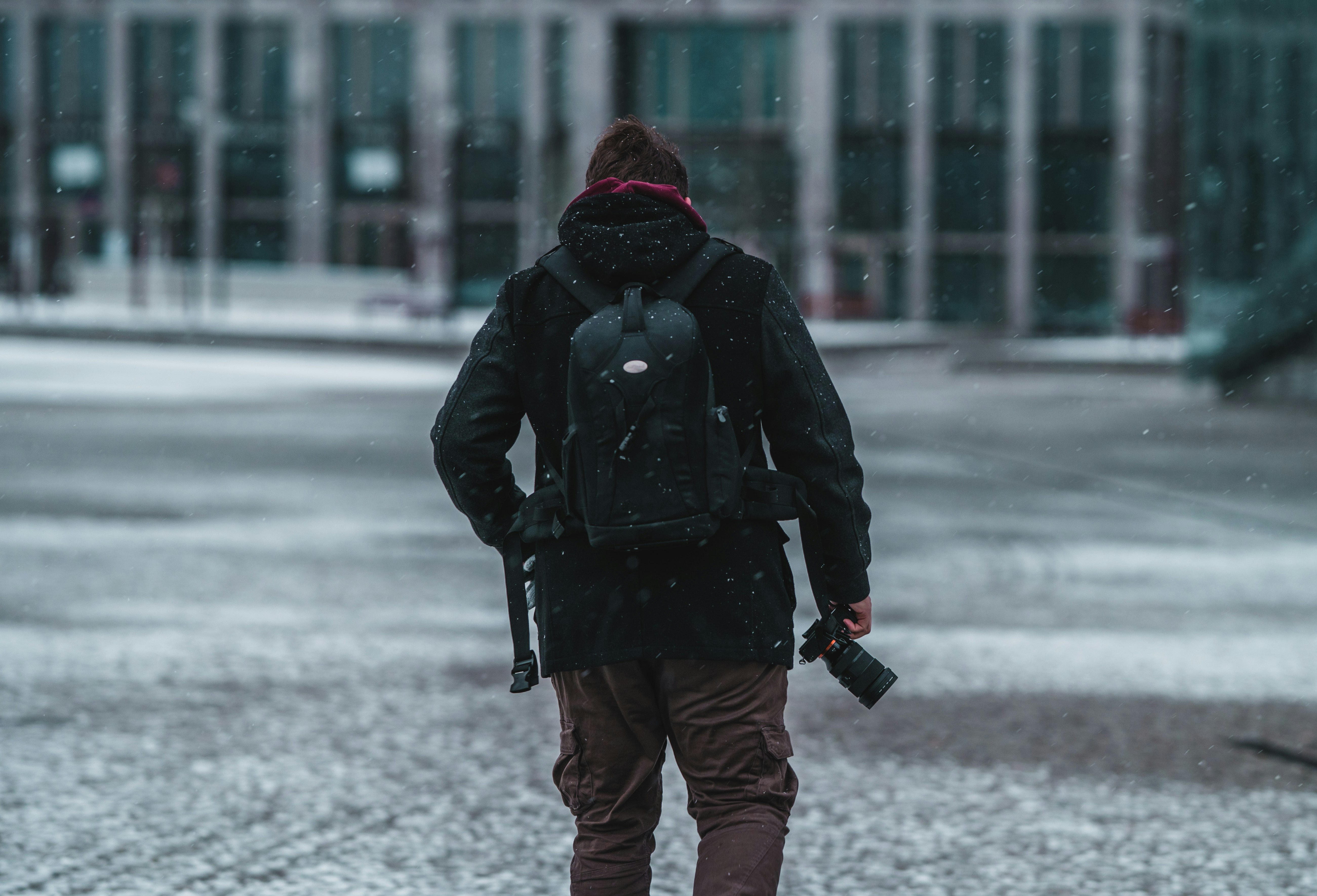 person in black jacket and red knit cap walking on snow covered ground during daytime